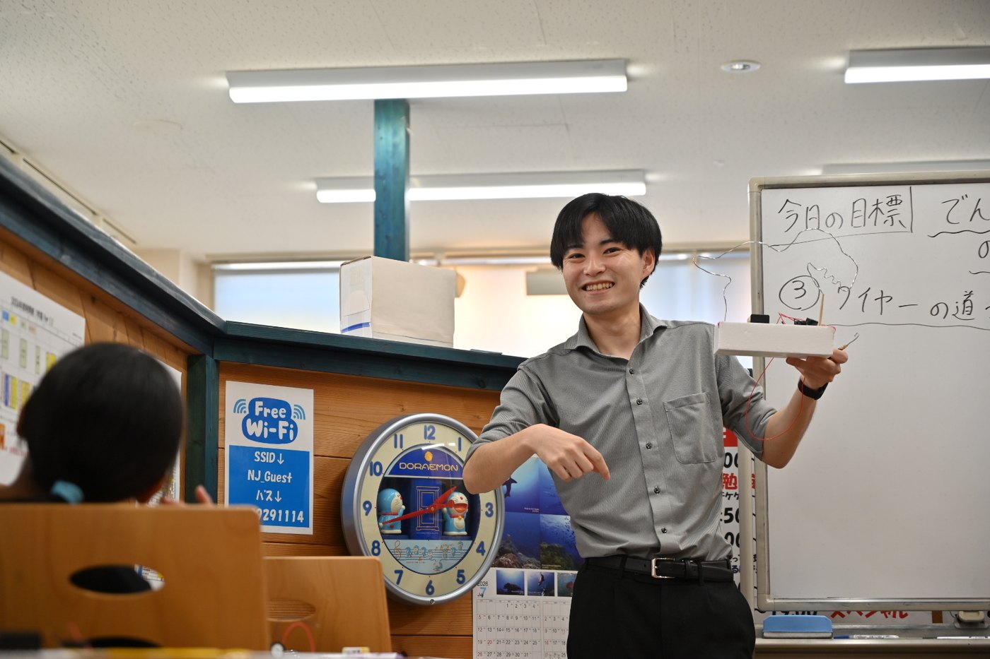 ホワイトボードの前でイライラ棒の本体を持って説明する忽那先生